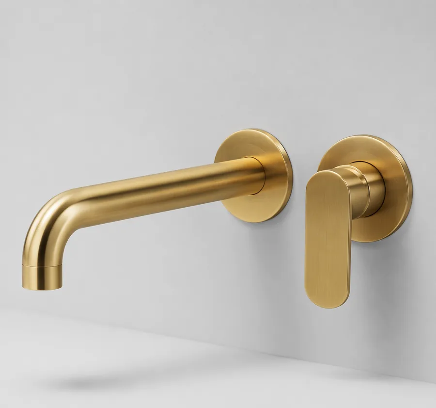 Arco brushed gold wall-mount basin faucet on light wall, studio product photo
